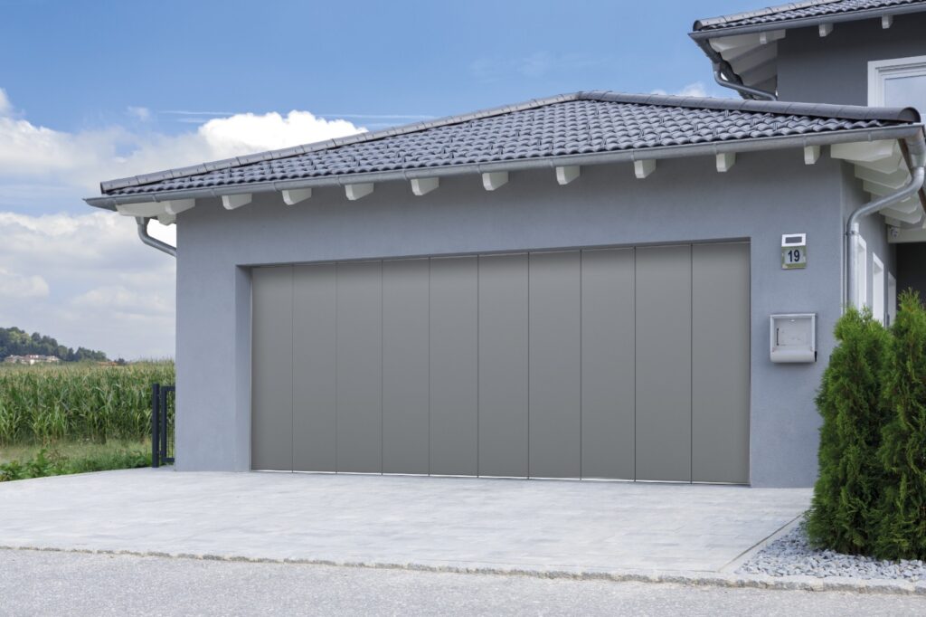 Portone garage sezionale Normstahl colore grigio, design moderno, installato su casa unifamiliare in contesto residenziale. Soluzioni Securplus.
